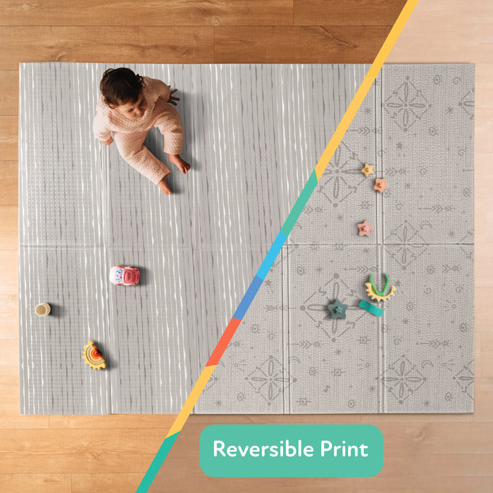 A split-image shows a baby playing on the Nuby US Reversible Floor Mat | Graceful Grey, featuring gray stripes on one side and a subtle geometric print on the other. Toys surround the mat, which is easy to wipe clean and labeled "Reversible Print.