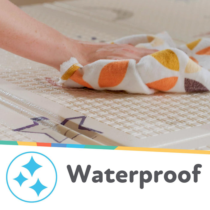 A hand easily wipes water off the textured Reversible Floor Mat | Graceful Grey by Nuby US with a colorful cloth. Below, a waterproof label featuring a blue sparkle icon is displayed on the mat.